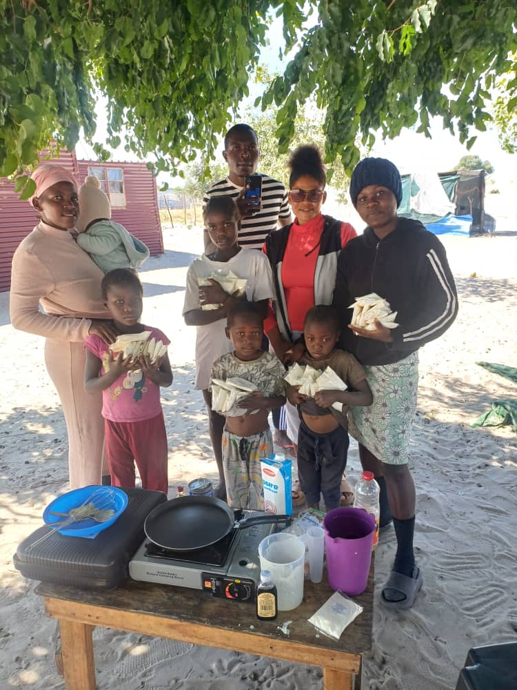Children, caregivers, and volunteers posing with cooking supplies outdoors.